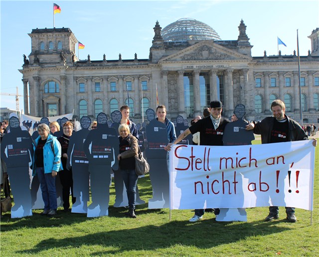 Menschen stehen vor dem Reichstagsgebäude in Berlin mit Pappfiguren und einem Banner mit der Aufschrift 'Stell mich an, nicht ab!!!'