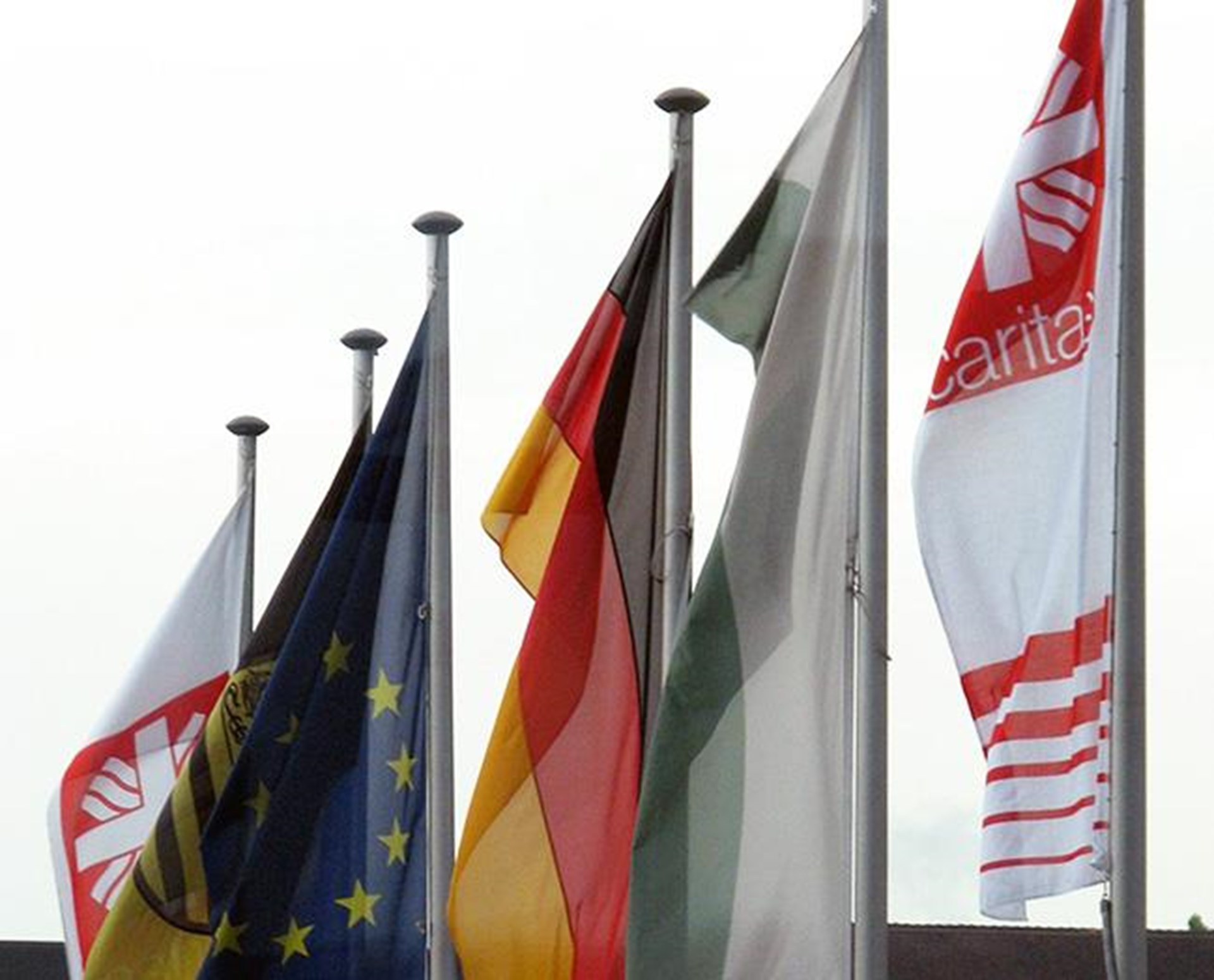 Fahnenmast mit wehenden Fahnen von Caritas, Deutschland und EU 
